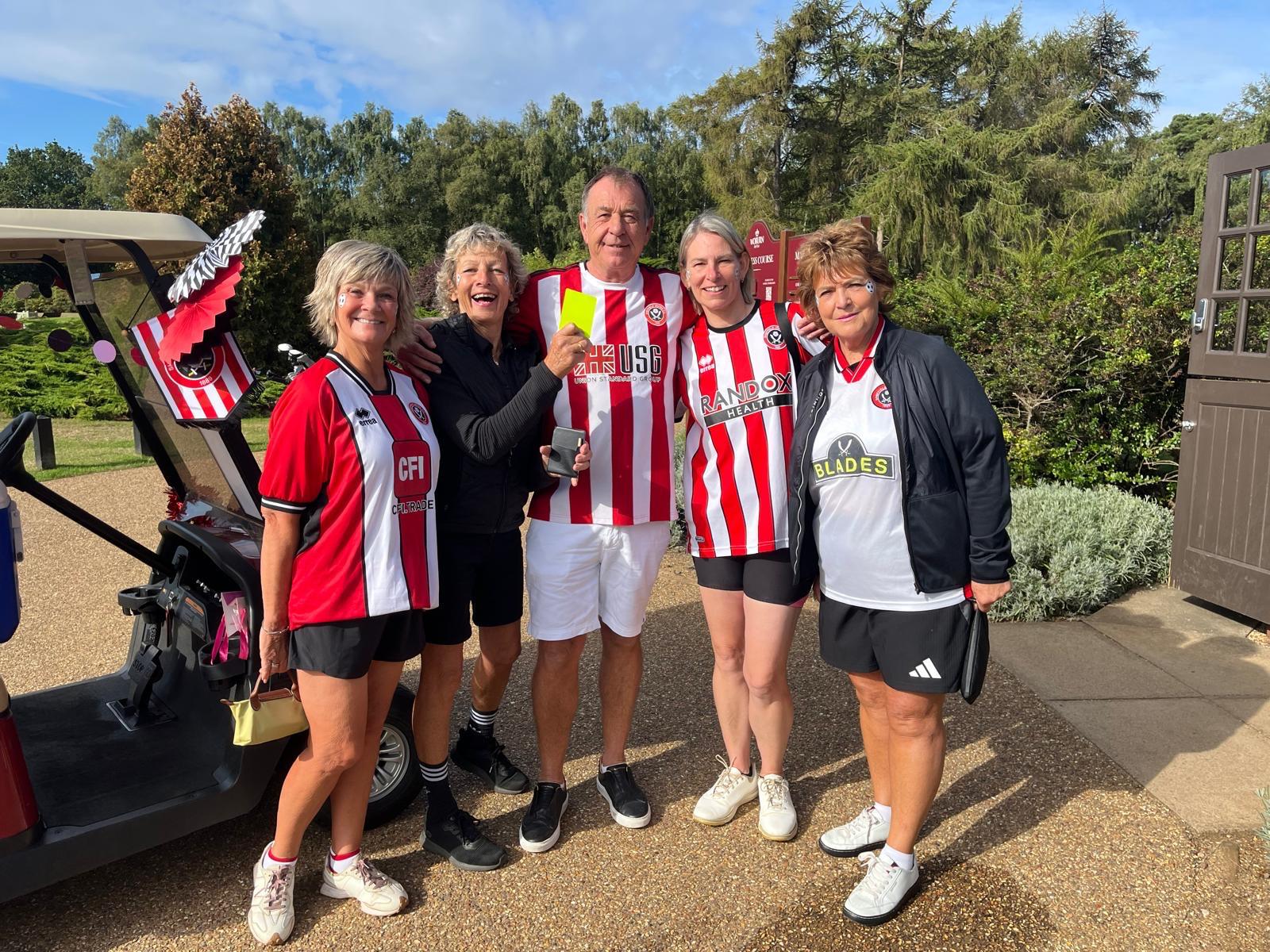 four ladies in football shirts standing with the captain in front of a golf bugy decorated with ballooons